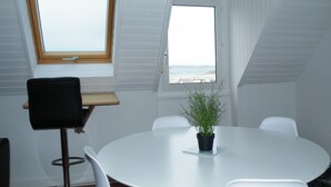 Una mesa redonda con sillas blancas, una pequeña planta en maceta y vista al mar a través de una ventana.