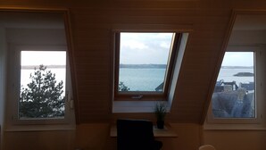 Una habitación con techo inclinado y dos ventanas que dan al mar.