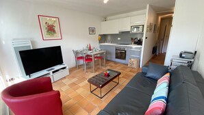 Sala de estar com televisão, sofá vermelho e preto, e um espaço de jantar com mesa e cadeiras.