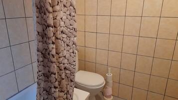 A bathroom with beige tiles, a toilet, and a shower curtain with a pebble pattern.