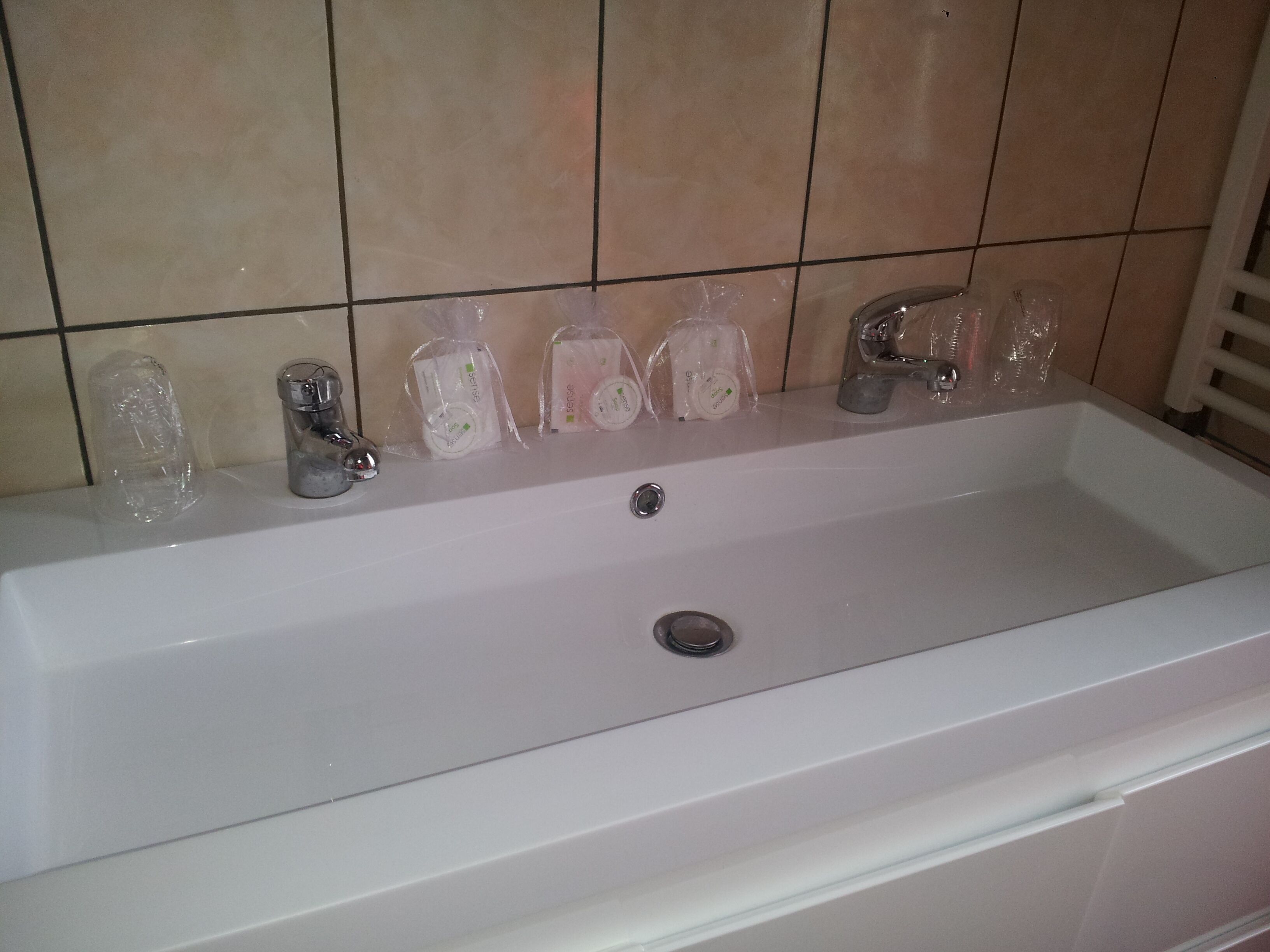 Pesualtaalla on peili, hana ja useita hygieniatuotteita muovipusseissa, jotka on asetettu pesualtaan reunalle.