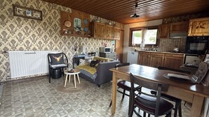 A cozy living area with a sofa, a dining table, and a kitchen area with wooden cabinets and a microwave. - L'Eterle de Motzon en Bauges: in the mountains, snow, skiing, hiking, relaxation... (Aillon-le-Jeune)