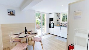 Eine moderne Küche mit weißen Schränken, einer Mikrowelle und einem Spülbecken. Ein Essbereich mit einem Tisch für zwei Personen, einer Weinflasche und einem Glas.