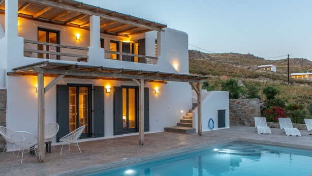 Eine moderne Villa mit Swimmingpool, Außenmöbeln und einer Treppe zu einem zweiten Stockwerk.
