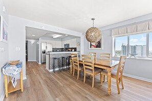 A modern kitchen with white cabinets, a central island, and a dining area with a wooden table and chairs.