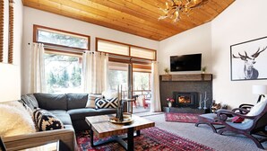 A cozy living room with a fireplace, a sofa, a coffee table, and a large window with curtains.