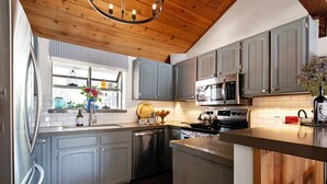 A modern kitchen with grey cabinets, stainless steel appliances, and a wooden ceiling.