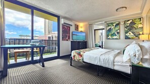 A hotel room with a bed, a desk with a chair, a TV, and a balcony with a view of buildings.