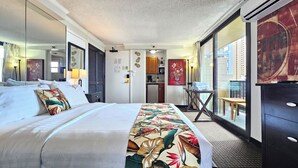 Ein Hotelzimmer mit Bett, einer kleinen Küchenzeile, einer Sitzecke mit Tisch und Stuhl sowie einem großen Fenster mit Blick auf die Stadt.