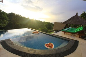 Una piscina con cuencos con forma de corazón, una tumbona y una estructura de techo de paja.