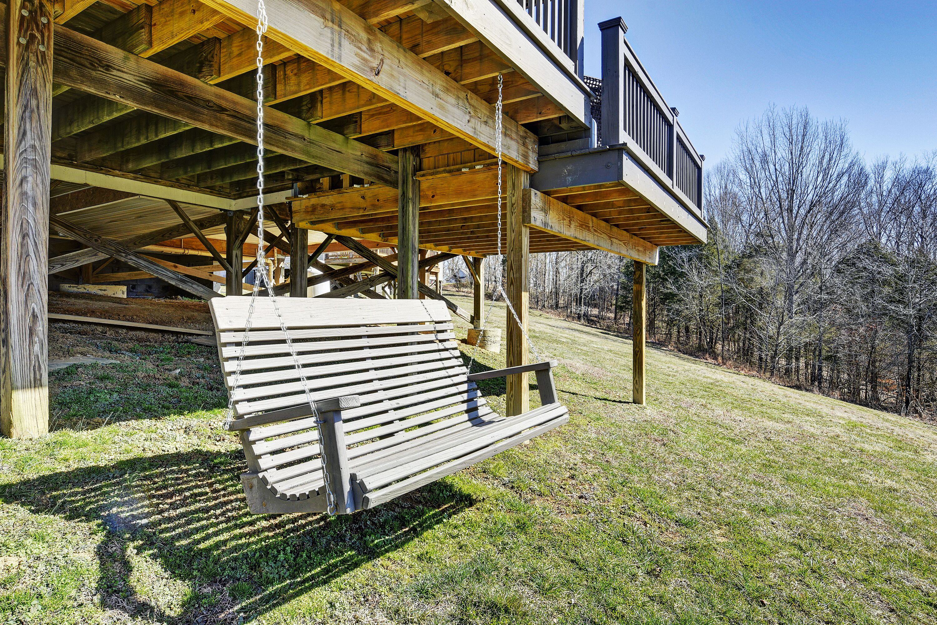 A wooden deck with a swing chair, a balcony, and a view of trees.