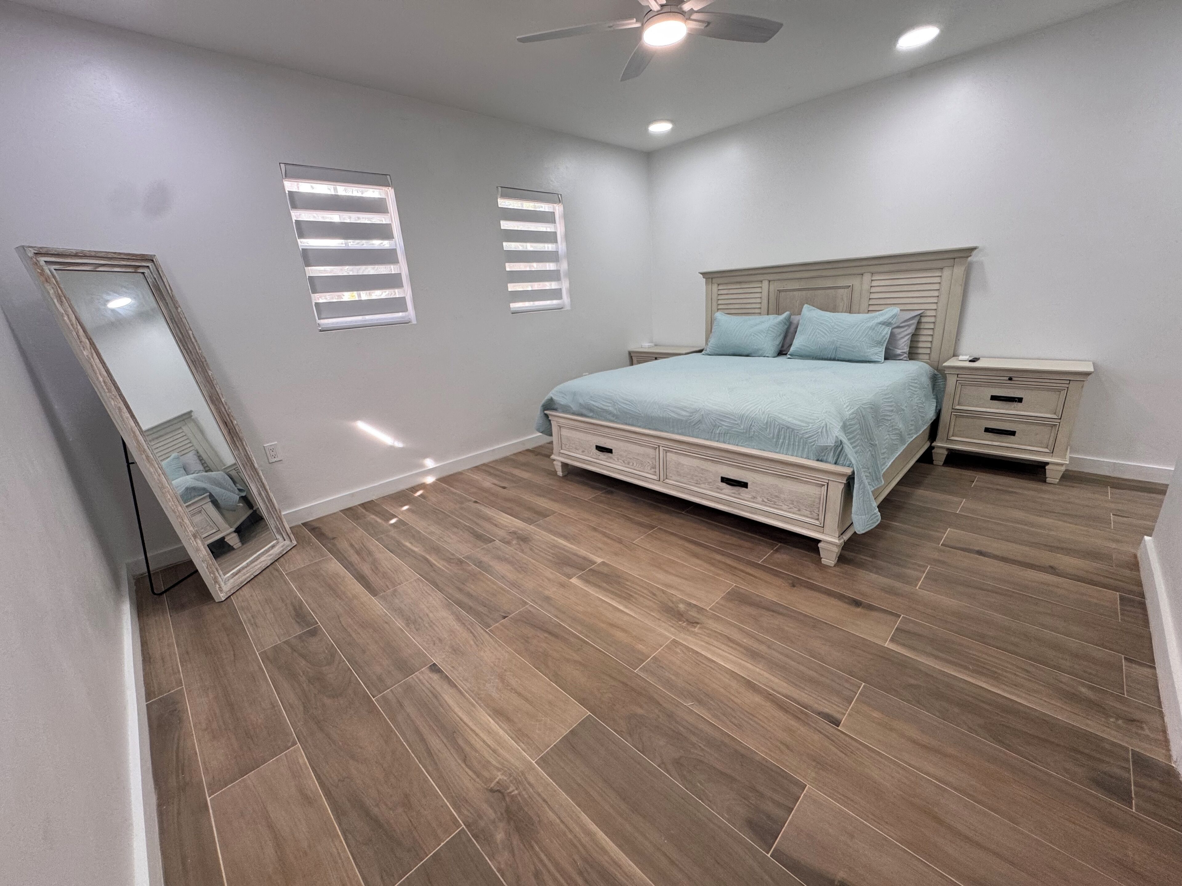 Une chambre à coucher avec un lit, des tables de chevet, un miroir et un ventilateur de plafond.