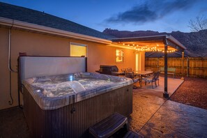 Ein Whirlpool mit einer Holzbank, einem Tisch mit Stühlen und Lichterketten in einem Garten.