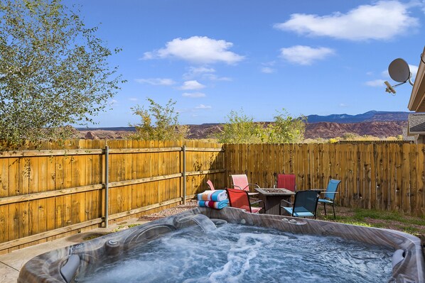 A backyard with a hot tub, wooden fence, and chairs.