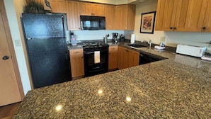 A kitchen with granite countertops, wooden cabinets, a black refrigerator, a microwave, a stove, and a toaster. - On the Promenade 1st floor. Spectacular Panoramic Ocean Views, Patio with grassy (Seaside)