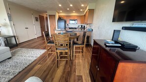 A modern living room with a dining area, wooden flooring, and a kitchen with wooden cabinets and a flat-screen TV. - On the Promenade 1st floor. Spectacular Panoramic Ocean Views, Patio with grassy (Seaside)