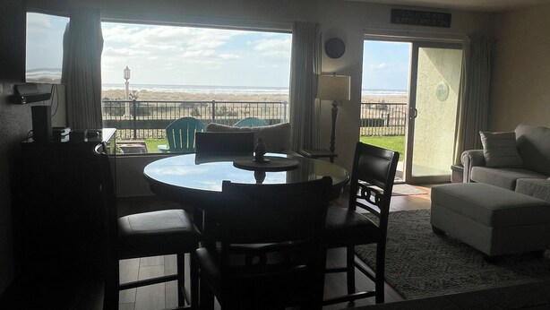 A room with a round table and chairs, a sofa, and a view of the beach through large windows. - On the Promenade 1st floor. Spectacular Panoramic Ocean Views, Patio with grassy (Seaside)