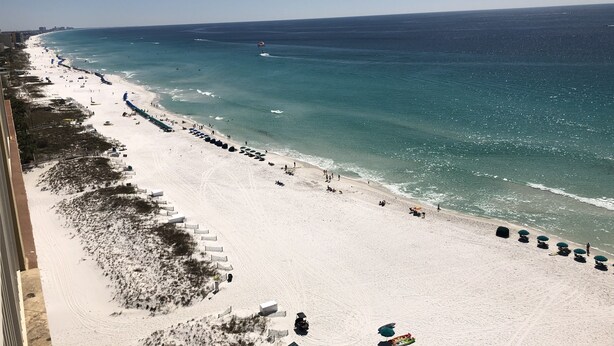 A beach with a long stretch of sand, a few umbrellas, and a few people. - GULF FRONT!!  Beautiful Sweeping Views! Tiki Bar, Deli, 3 pools, LOCATION (Destin)