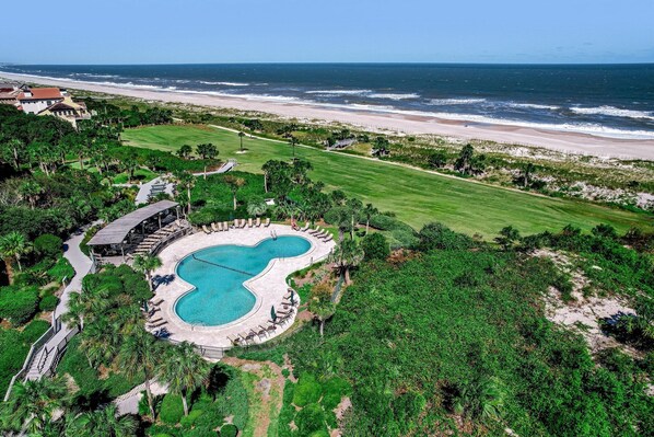 An aerial view of a resort with a swimming pool, beachfront, and lush greenery.