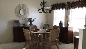 Un coin repas avec une table ronde entourée de chaises en osier, un lustre et un miroir décoratif accroché au mur.