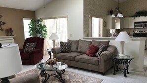 Un salon comprenant un canapé, un fauteuil, une table basse en verre et un tapis à motifs.