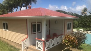 Une maison avec un toit rouge, une véranda dotée de balustrades blanches et un petit jardin devant.