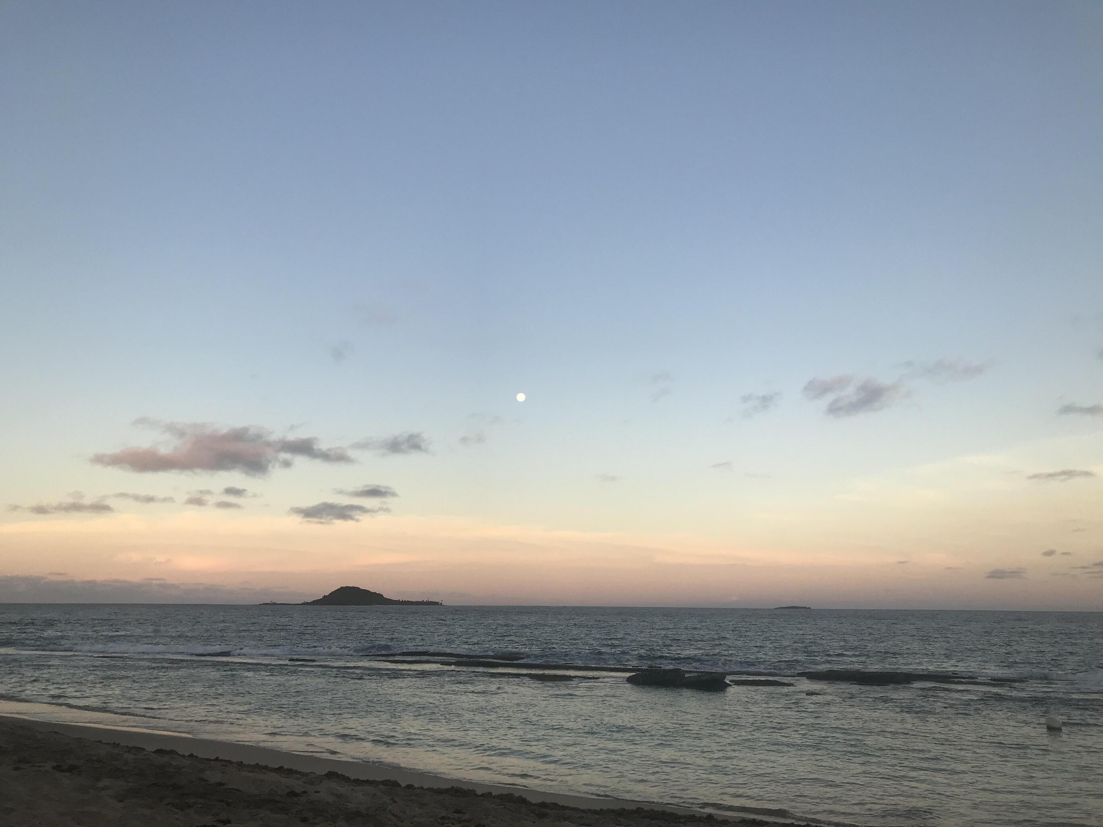 Una playa con aguas tranquilas, una isla distante y cielo despejado.