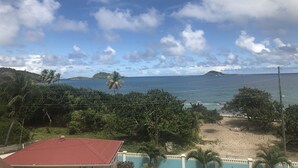 Une vue sur la côte, avec un bâtiment à toit rouge, des palmiers et une plage de sable.