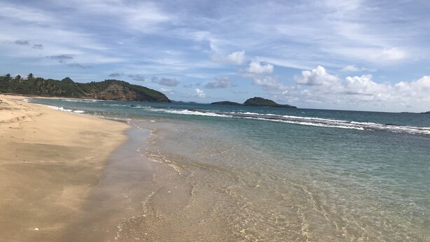 Une plage à l’eau claire, avec un rivage sablonneux et des îles qui se dessinent à l’horizon.