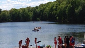 A lakeside scene with people near the water, boats, and a forested area in the background. - Mountainside Spa With View’s  (Bushkill)