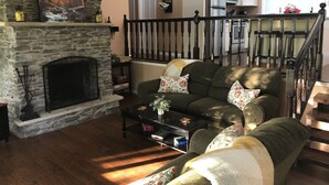 A living room with a stone fireplace, a sofa set, a coffee table, and a staircase leading to a kitchen. - Mountainside Spa With View’s  (Bushkill)