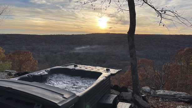 A hot tub in a natural setting with a view of a forested landscape and a sunset in the background. - Mountainside Spa With View’s  (Bushkill)