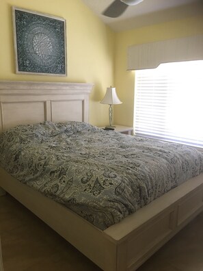 A bedroom with a bed, a nightstand, a lamp, a window with blinds, and a decorative wall piece. - <br>Partial Ocean View 2BR 2BATH<br>Sleeps 4. (Fort Myers Beach)
