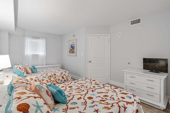 A bedroom with a bed, a TV, a dresser, and a window with blinds.