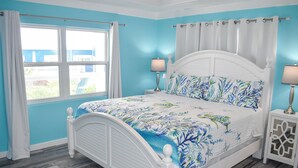 Une chambre à coucher avec un lit blanc, des murs bleus et une fenêtre avec des rideaux.
