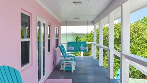 Une véranda couverte avec des fauteuils Adirondack de couleur turquoise et un bâtiment rose.