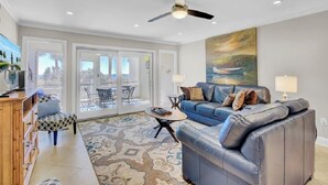 A modern living room with a blue leather sofa, a wooden cabinet, and a patterned rug. - Award-Winning Resort Amenities | Beach Club Villa 12 (Isle of Palms)