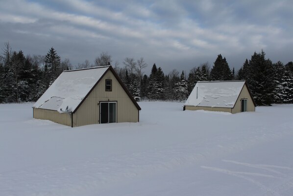 Two small, single-story buildings with sloped roofs, surrounded by snow-covered ground and trees. - Delightfully a Frame Cabin #2 (Munising)
