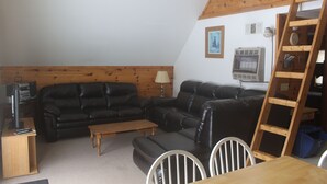 Een gezellige woonkamer met een zwarte leren bank, een houten salontafel en een eettafel met stoelen.