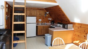 Een compacte keuken met houten kastjes, een koelkast, een magnetron en een fornuis. Er is een ladder die leidt naar een slaapgedeelte boven.
