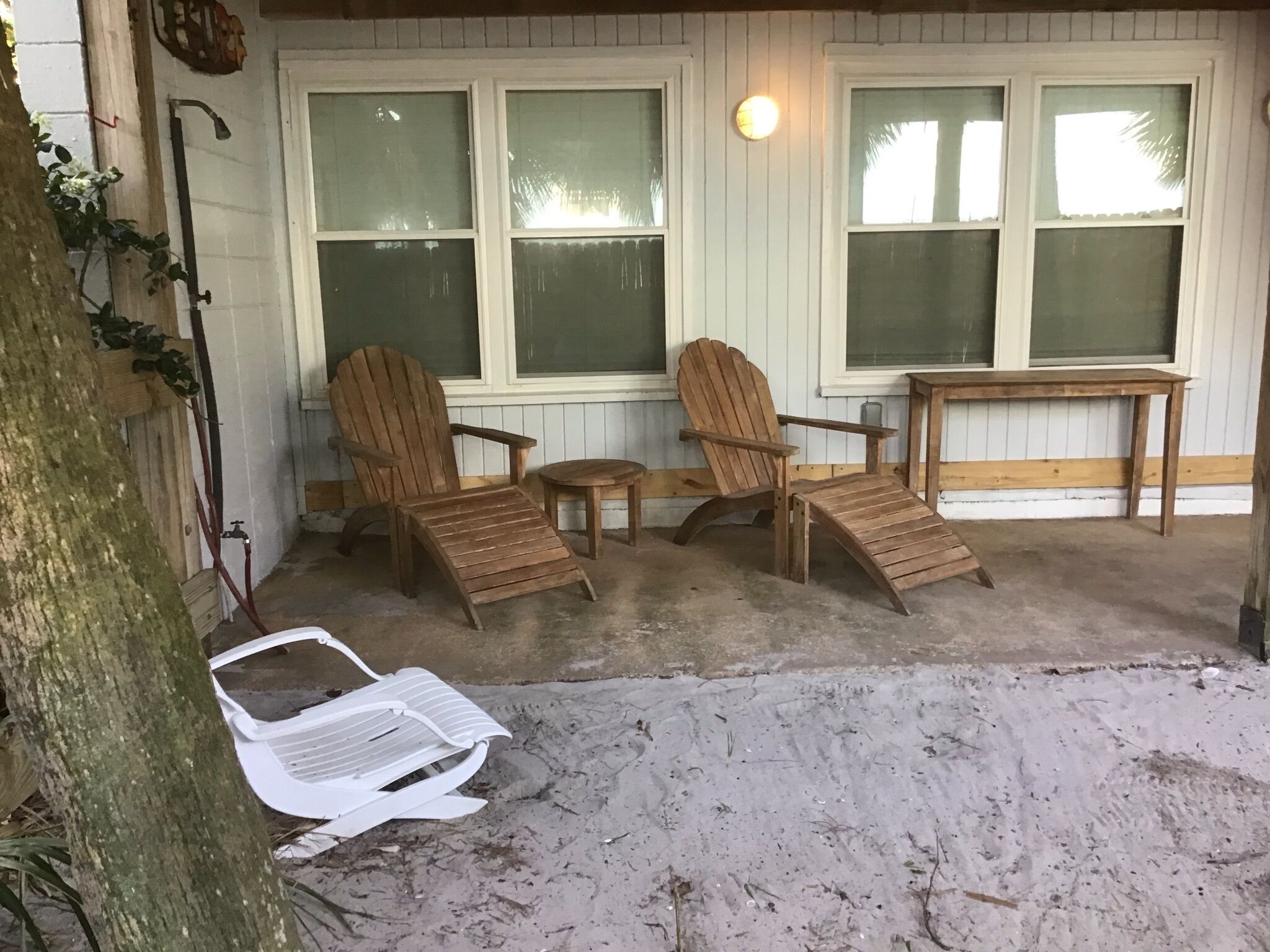 Un porche abrité avec deux fauteuils Adirondack, une petite table ronde et une chaise en plastique blanche.