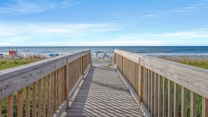 Ein hölzerner Steg führt zu einem Strand, im Hintergrund ist ein Rettungsturm sichtbar.
