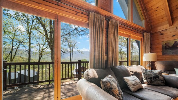 Uma cabana de madeira com uma janela grande, um sofá estofado com almofadas decorativas e um quadro de ursos na parede.