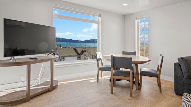 Ein modernes Wohnzimmer mit einem großen Flachbildfernseher, einem runden Esstisch mit Stühlen und einer Couch. Große Fenster bieten Blick auf das Meer und die Berge.