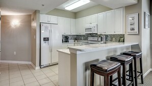 A modern kitchen with white cabinets, a built-in microwave, and a large island with bar stools. - 3rd Floor Marina View. Hot Tubs, Pool, Near Golf | Barefoot North Tower - 301 (North Myrtle Beach)