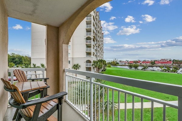 A balcony with a view of a green field and a tall building.