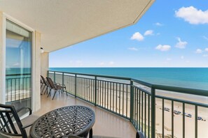 Ein Balkon mit Blick auf den Strand, einem Tisch und Stühlen.