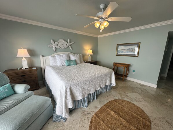 A bedroom with a bed, nightstands, a ceiling fan, a wall clock, a framed picture, and a woven rug.