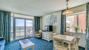 A hotel room with a balcony, a dining area, a sofa, a TV, and a dresser.