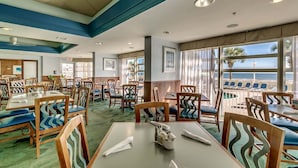 A restaurant with tables and chairs, large windows with a view of the ocean, and a ceiling with recessed lighting.